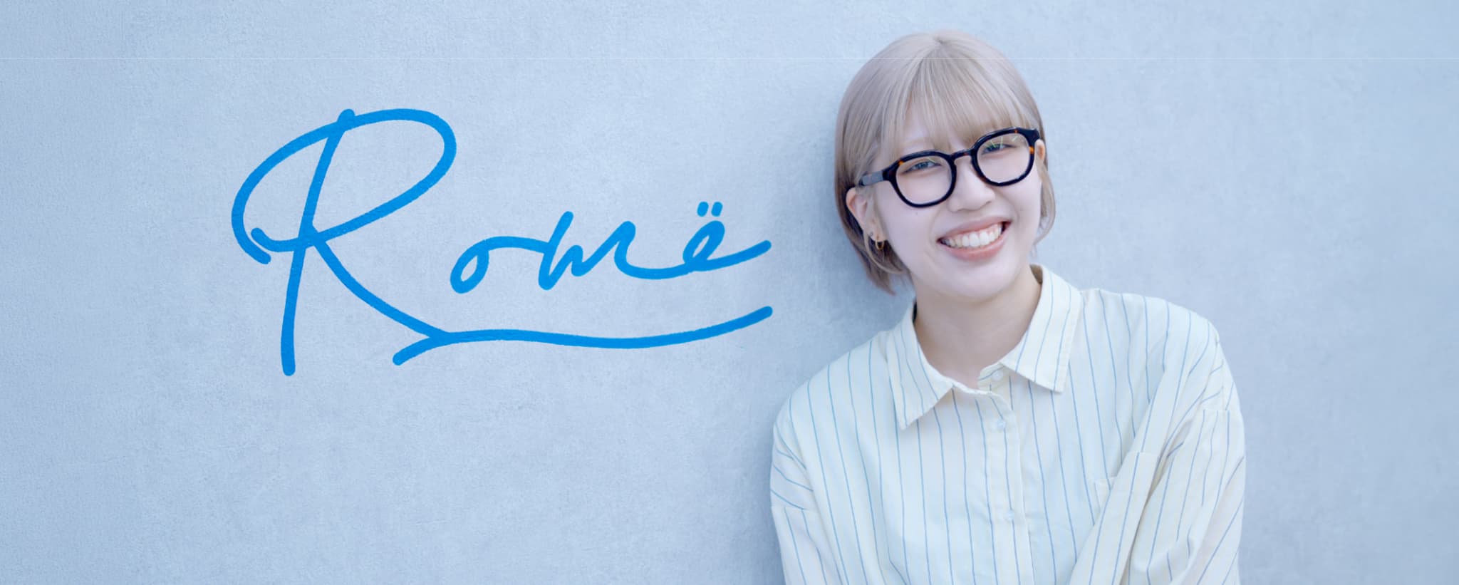 Romëのロゴ壁の前に立つ菜里